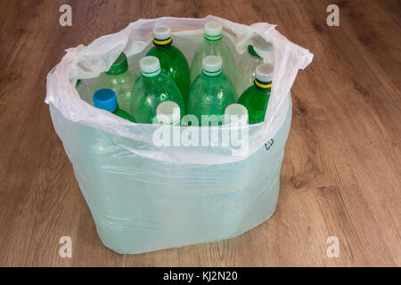 Green plastic bottles on wooden floor. Ecological separation of household waste. Empty pet bottles in a plastic bag. Stock Photo