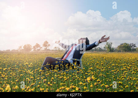 Asian businessman is lying on a chair and open his arm in a large yellow flower field Stock Photo