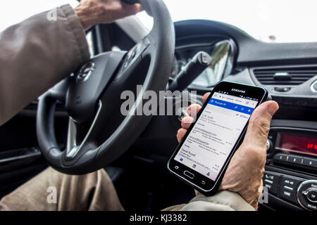 Irresponsible man at steering wheel checking messages on smart phone / smartphone / cellphone while driving car on road Stock Photo