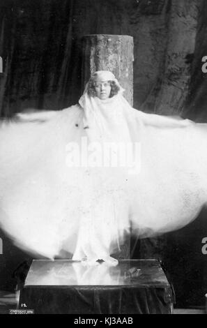 A photographic full length portrait of Loie Fuller, for the portrait she was standing still while moving the fabric of her white costume during the exposure, she stood on top of a mirror and was brightly lit, she was an American dancer who is considered a pioneer of modern dance and theatrical lighting techniques, 1896. From the New York Public Library. Stock Photo