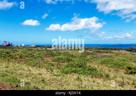 Green coastal vegetation against sea and distant Umhlanga city skyline with blue cloudy sky landscape view from the ridge in Durban, South Africa Stock Photo