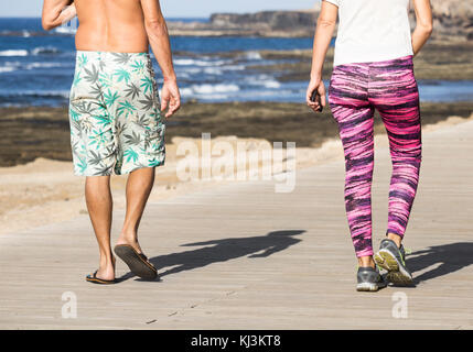 Rear view of of man and woman walking on coastal boardwalk in Spain Stock Photo