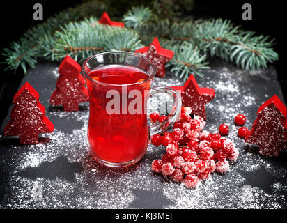 tea from fresh red viburnum in a transparent glass on a black background, near branch with red berries of viburnum in sugar