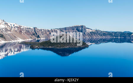Clear blue water of Crater Lake National Park in Oregon during early spring with some snow left from winter. Wizard Island in the distance. Stock Photo