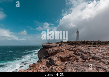 Cape Nelson lighthouse standing on a rugged cliff above ocean under stormy skies. Victoria, Australia