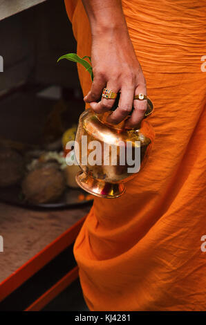 Priest in orange dhoti holding a copper kalash in his right hand with puja preparations in the background, Patit Pavan Sri Ram Mandir, Belgavi, Karnat Stock Photo