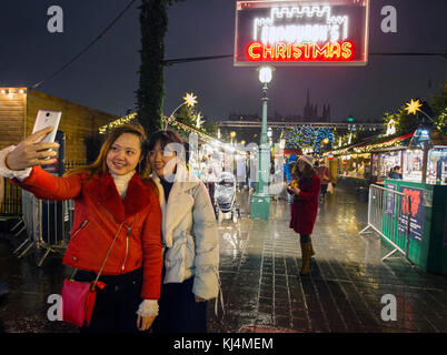 Two tourists take a selfie outside the Edinburgh Christmas market on Princes Street Edinburgh. Stock Photo