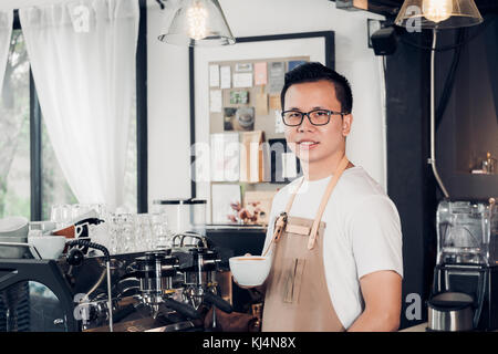 Male Barista cafe owner holding coffee cup in store counter bar inside coffee shop, food and drink business start up. Stock Photo