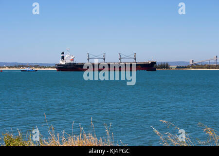 Large container ship entering channel to Bunbury Inner Harbour Western Australia aided by tug boat on a fine afternoon in summer. Stock Photo