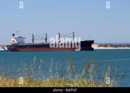 Large container ship entering channel to Bunbury Inner Harbour Western Australia aided by tug boat on a fine afternoon in summer. Stock Photo