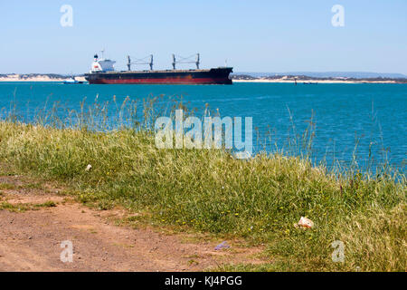 Large container ship entering channel to Bunbury Inner Harbour Western Australia aided by tug boat on a fine afternoon in summer. Stock Photo