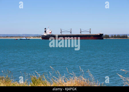 Large container ship entering channel to Bunbury Inner Harbour Western Australia aided by tug boat on a fine afternoon in summer. Stock Photo