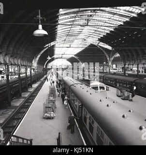 1950s, historical picture showing the Victorian train shed with glazed roof at London's Paddington Railway Station, with trains waiting for boarding passengers at platforms, Praed Street, London, England, UK.