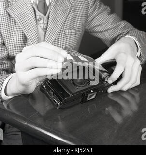 1950s, historical, young man loading negative roll film into the back of a film camera. This spool-wound photographic had paper backing which protected the film from white light exposure. Roll film was the popular film choice at this time. Stock Photo