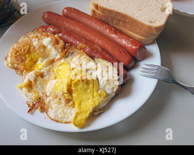 Fried eggs and sausages with bread on white dish close up Stock Photo