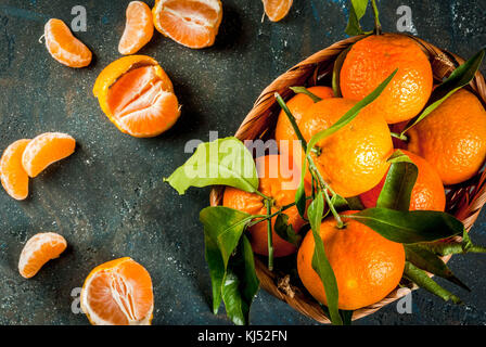 Fresh raw organic Tangerines with green leaves in little basket on dark concrete stone background, copy space Stock Photo