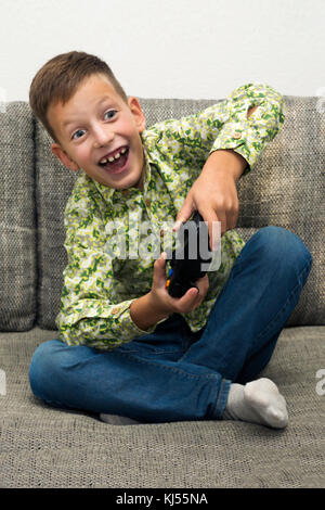 Boy playing video games with joystic sitting on the sofa Stock Photo