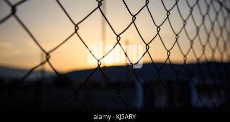 Steel wire mesh fence on a sunset background. Blurred smokestacks and mountains silhouette. Stock Photo
