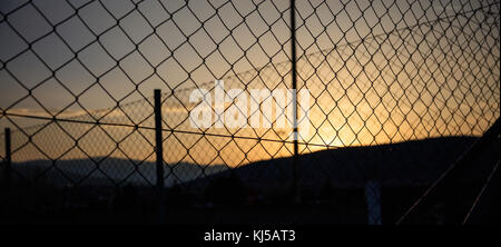 Steel wire mesh fence on a sunset background. Blurred city and mountains silhouette. Stock Photo