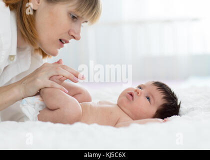 Mother and child on white bed. Parent and little kid relaxing at home. Mom doing massage baby. Stock Photo