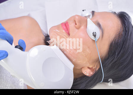 Beautiful young woman lying on a table with protect glasses on eyes getting a laser skin treatment Stock Photo