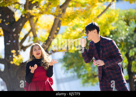 Young asian couple blowing bubbles in autumn scene Stock Photo