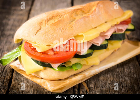 Big sandwich stuffed with ham,cheese and vegetables on the wooden table Stock Photo