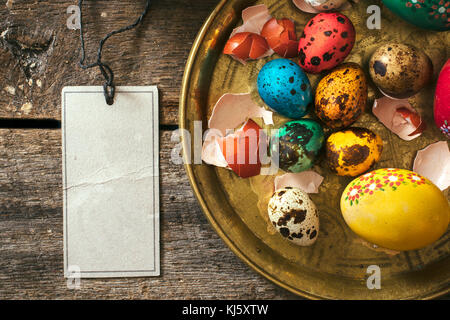 Decorative Eastern eggs in the plate and blank card on wooden background Stock Photo