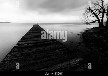 Long exposure first person view of a pier on a lake, with a tree and perfectly still water Stock Photo