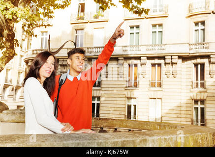 Happy young couple standing at the embankment of Seine River and pointing to the Eiffel Tower, walking along Paris, France Stock Photo