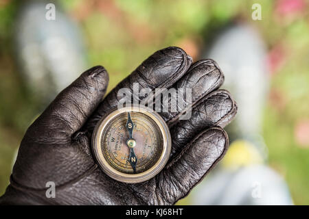 Man's hand in a leather glove holding a compass. Nature background. Stock Photo