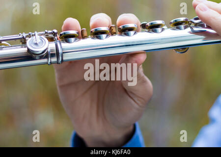 Detail of a male fingers playing a transverse silver flute, outdoors, closeup. Stock Photo