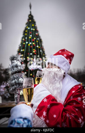 Celebration and New Year concept. Man with beard holds champagne glass. Guy near Christmas tree in the park. Santa Claus in red hat. Happy new Year! Stock Photo