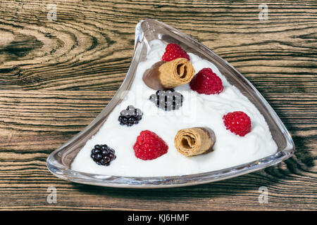 Sweet temptation with fresh fruits and biscuits. Glass bowl with yogurt, raspberries and blackberries on wooden background. Stock Photo