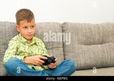 Boy playing video games with joystic sitting on the sofa Stock Photo
