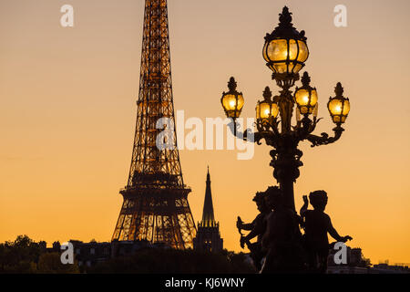 Alexandre III Bridge lamp post silhouette contrasting with the Eiffel Tower at sunset. Paris, France