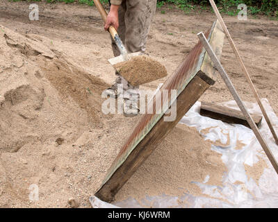 Construction worker sifting gravel through a sieve with shovel. Stock Photo