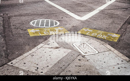 Yellow-ish and graphic signs on the asphalt to warn pedestrians to look right and left before crossing the street. Stock Photo