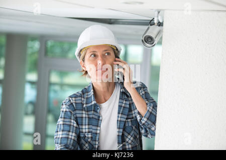 female technician on the phone fitting cctv camera Stock Photo