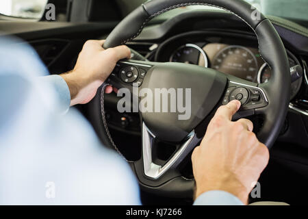 Close up of man sitting in the driver seat, pressing a buttons on steering wheel, view from behind the driver Stock Photo