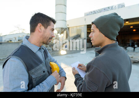 Man taking notes from worker on factory site Stock Photo