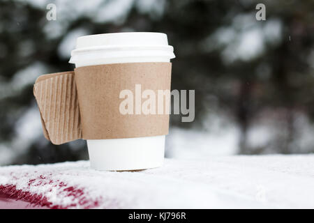 Steaming Cup of Hot Coffee or Tea standing on the Outdoor Table in Snowy Winter Morning. Cozy Festive paper cupwith a Warm Drink in Winter Garden. Chr Stock Photo