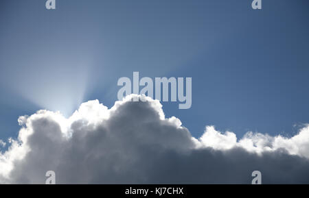 sun rays shining from behind a thick cloud on clear blue sky Stock Photo