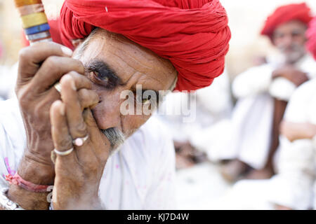 Member of ethnic minority - elder Rabari man in red turban smoking clay pipe. Photo taken at countryside near Jodhpur, Rajasthan, India. Stock Photo