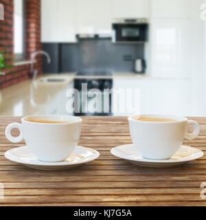 Empty kitchen wooden table top with two coffee cups, modern kitchen in background Stock Photo