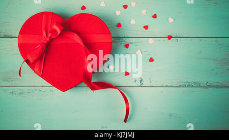 Valentines heart shaped present with a ribbon and red candies on aquamarine wooden planks. Top view Stock Photo