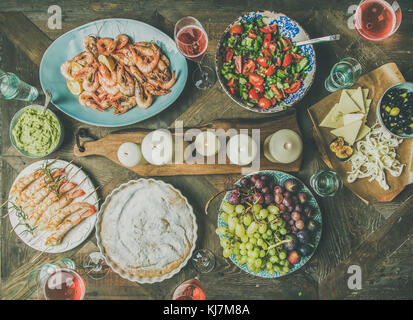 Holiday celebration table setting with snacks. Flat-lay of salad, shrimps, olive, grape, homemade cake over wooden background, top view Stock Photo