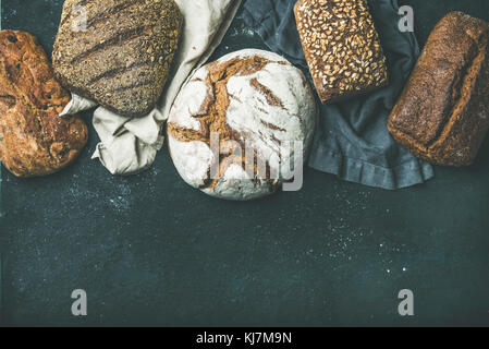 Various bread selection flat-lay. Top view of Rye, wheat and multigrain rustic bread loaves over black background, copy space Stock Photo