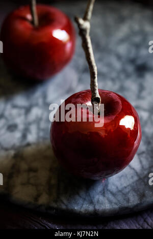 Detail shot of shiny, red, candy apple with twig stick on a marble tray. Moody, dark feel. Stock Photo