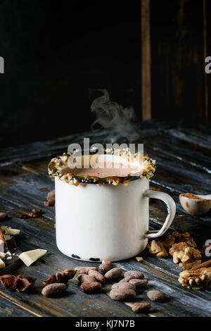 Vintage mug of hot chocolate, decor with nuts, caramel, spices. Ingredients above. Chopped dark and white chocolate, cocoa beans, anise over old woode Stock Photo